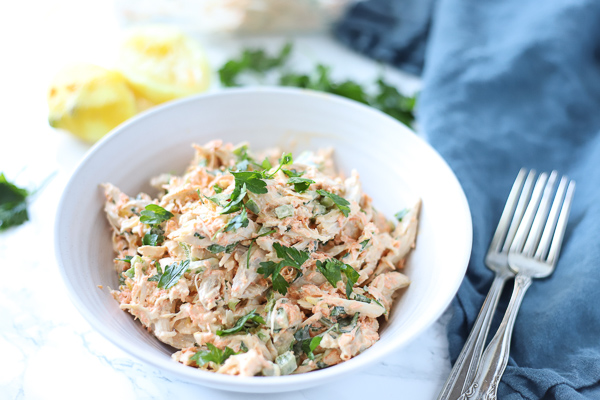 healthy chicken salad in a white bowl with lemons behind it