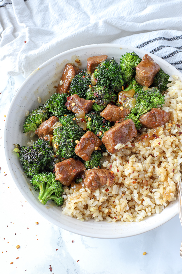instant pot beef and broccoli in a white bowl with a white and black striped towel