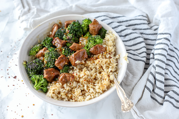 beef and broccoli over rice in a white bowl