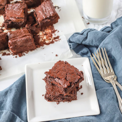 two healthy brownies stacked on a white plate on a blue napkin with two vintage forks to the right