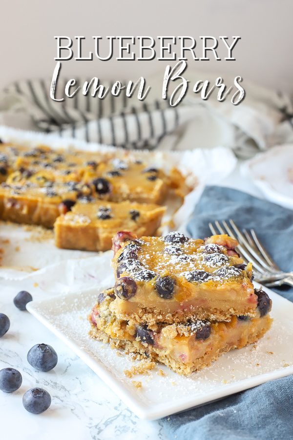 Two blueberry lemon bars stacked on a white place with a blue napkin to the right