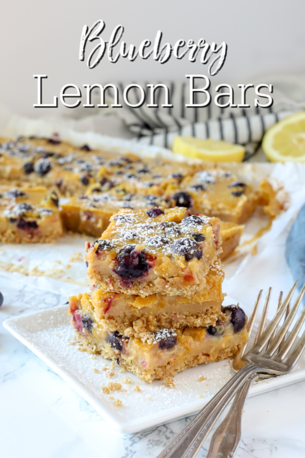 3 blueberry lemon bars stacked up on a white plate with antique forks to the right