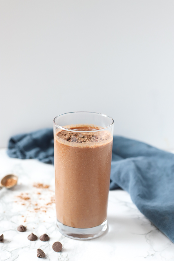 chocolate cauliflower smoothie in a glass cup with chocolate chips and cocoa powder around it