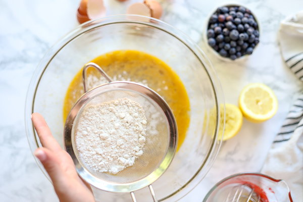 sifting flour into lemon curd to make blueberry lemon bars