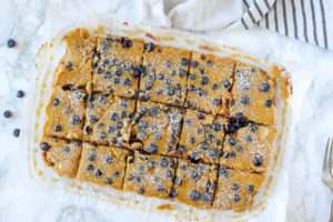 blueberry lemon bars sliced on white parchment paper with a black and white stripped towel behind it.