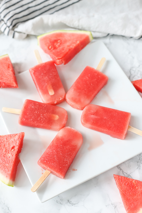 watermelon popsicles on white plate with watermelon slices around it