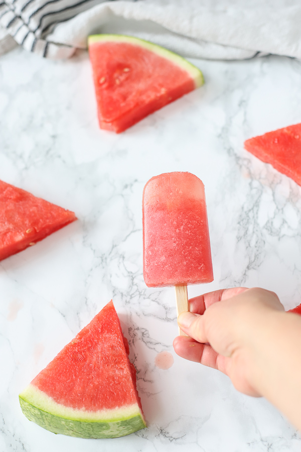 hand holding watermelon popsicles with watermelon in the backgrond