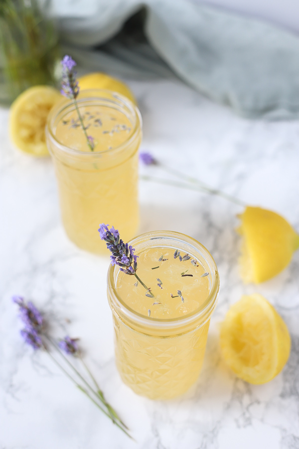 2 glasses of lavender lemonade with lemons ad fresh lavender around it