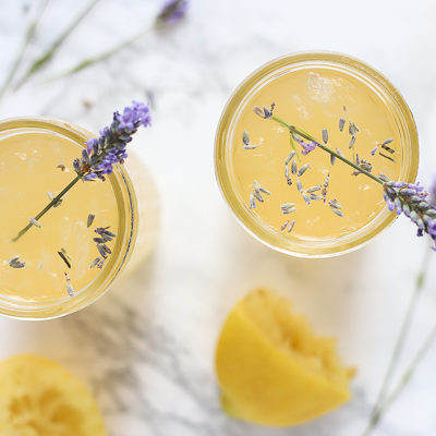 overhead shot of two glasses of lavender lemonade with dried lavender sprinkled in and a sprig of fresh lavender