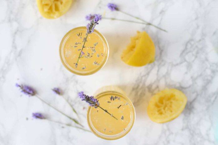 Overhead photo of two glasses of lavender lemonade with fresh sprigs of lavender int he glasses. The glasses are surrounded by a halved lemon and more lavender.