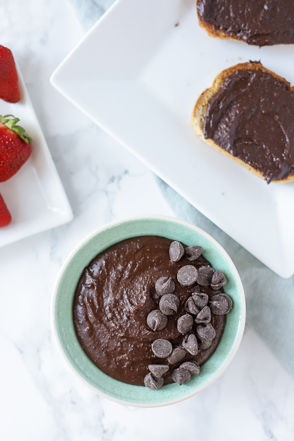 overhead shot of brownie batter hummus in a turquoise bowl and topped with chocolate chips. Two pieces of toast smothered with chocolate hummus to the back right of the bowl