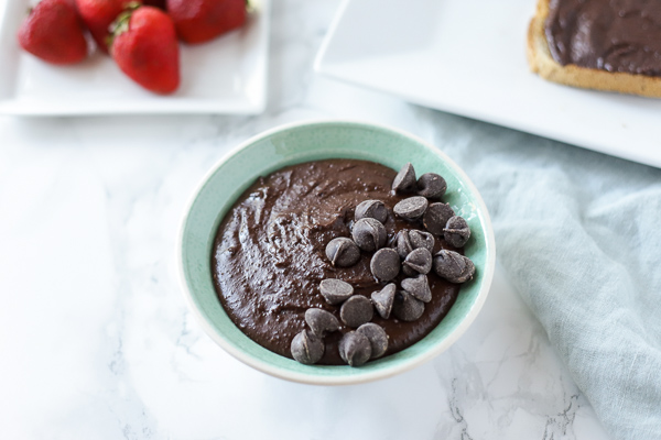 bowl of brownie batter hummus with a plate of strawberries and toast with chocolate hummus behind it