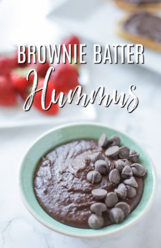 bowl of brownie batter hummus topped with chocolate chips with strawberries behind it