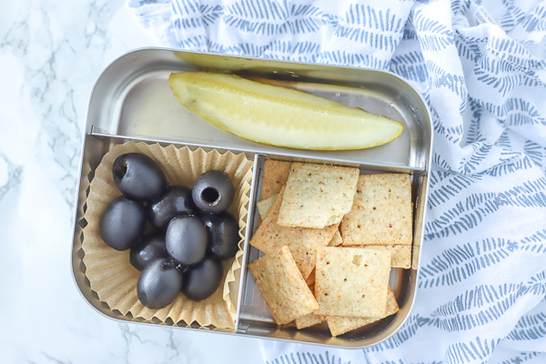 bento box with crackers, olives, and a pickle