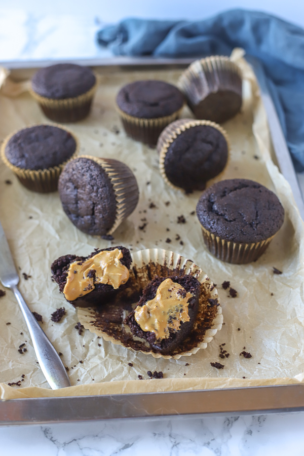 muffins on a baking sheet with one muffin sliced and spread with almond butter