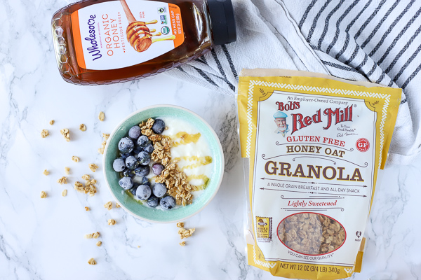 bowl of yogurt with granola and blueberries with package of honey and granola to the sides