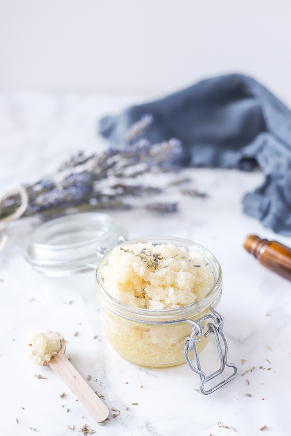 jar of diy foot scrub in a glass jar with a lid, a wooden spoon to the left and a bottle of essential oils to the back right