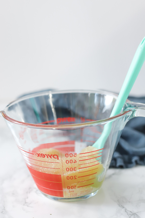 glass pryex measuring cup with diy foot scrub ingredients and a spoon to stir