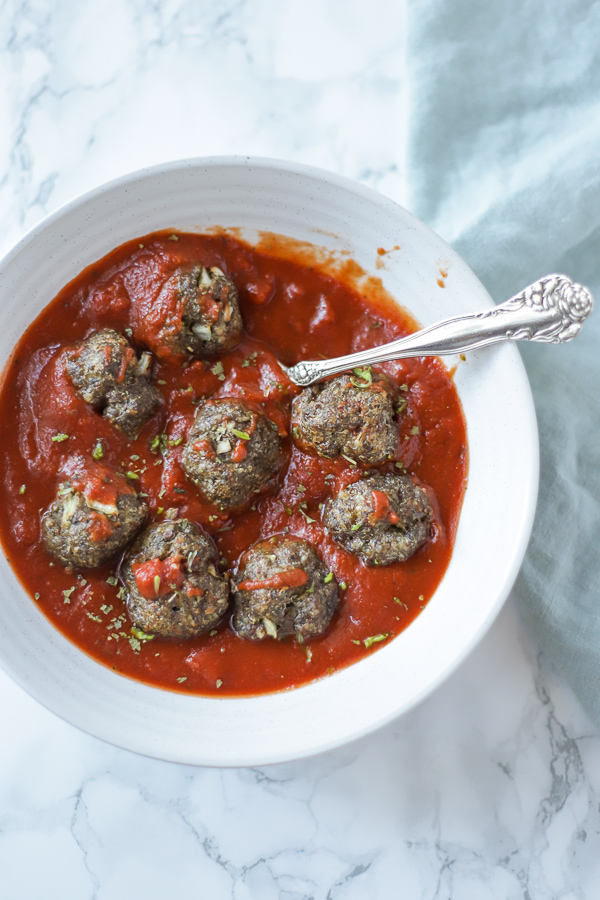 paleo meatballs in marinara sauce in a white bowl on a marble countertop with a teal napkin to the right