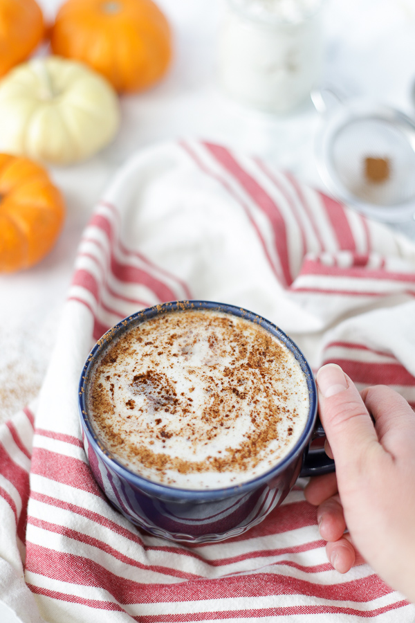 hand holding a blue mug with a frothy vegan pumpkin spice latte