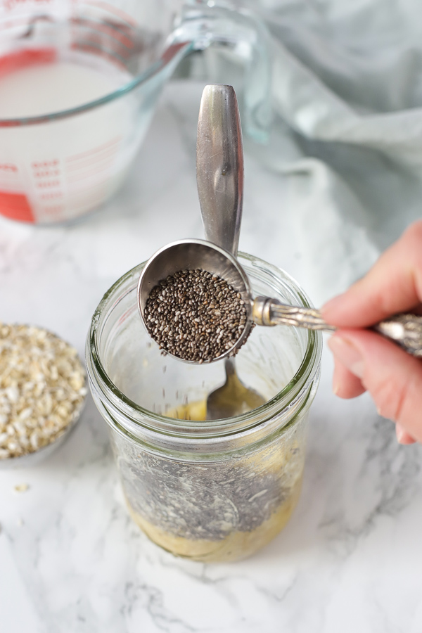 adding chia seeds to a mason jar with mashed banana for overnight oats