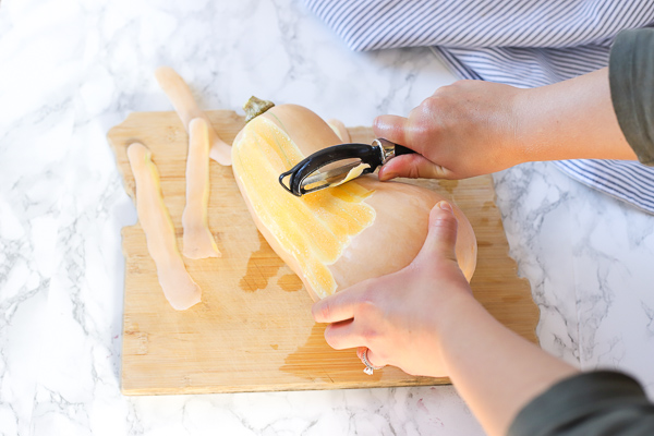 peeling butternut squash on a wood cutting board with a vegetable peeler