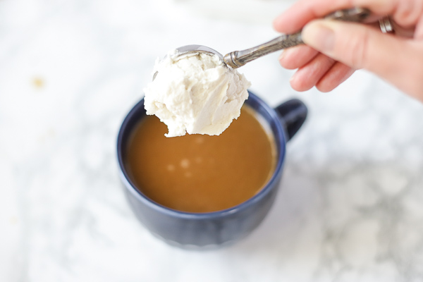 adding a large spoonful of vegan whipped cream into a vegan pumpkin spice latte