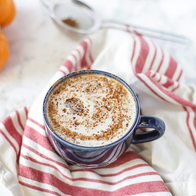 vegan pumpkin spice with a frothy top in a blue mug on top a tan and red stripped towel