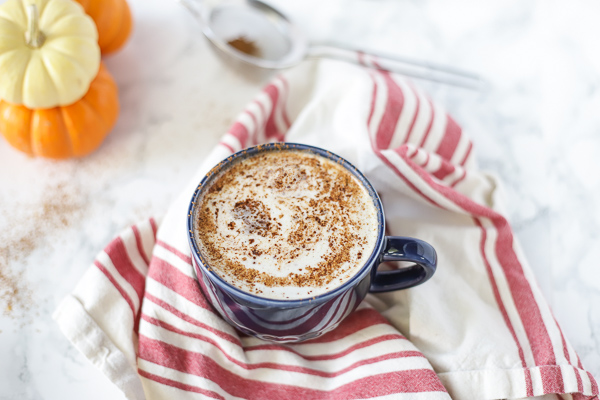 vegan pumpkin spice with a frothy top in a blue mug on top a tan and red stripped towel