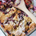 blackberry cobbler drizzled with cream fresh out of the oven with a wooden spoon ready to serve some delicious dessert