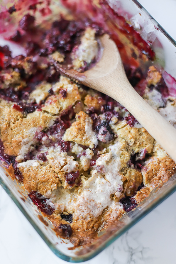 blackberry cobbler drizzled with cream fresh out of the oven with a wooden spoon ready to serve some delicious dessert