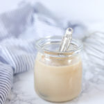 glass jar of homemade sweetened condensed milk with a antique silver spoon coming out. a blue and white stripped towel is in the background