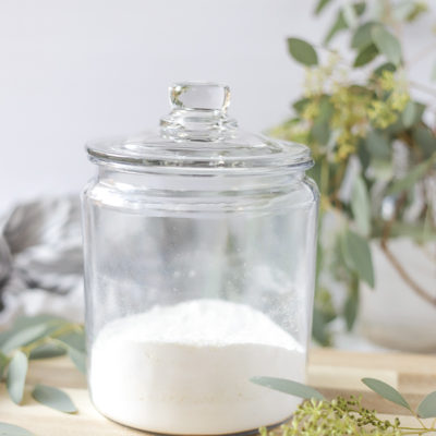 homemade laundry detergent in a glass dish with a lid on a wood cutting board with a mason jar full of eucalyptus