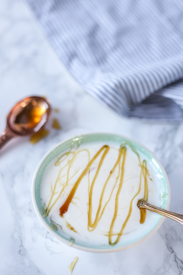 homemade yogurt in a teal bowl with honey drizzled on top. A copper table spoon with honey is in the background
