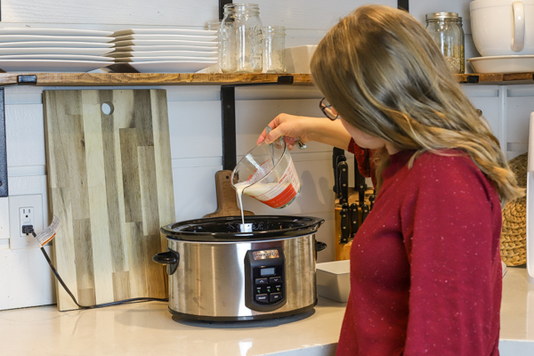 women in a red sweating pouring milk yogurt mixture into a crock-pot to make homemade yogurt