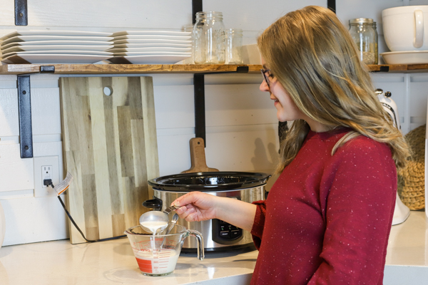 women adding yogurt starter to milk in a pyrex measuring cup to make homemade yogurt