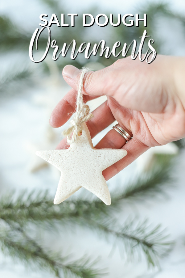 hand holding homemade salt dough ornaments in the shape of a star with twine. Evergreens are in the back