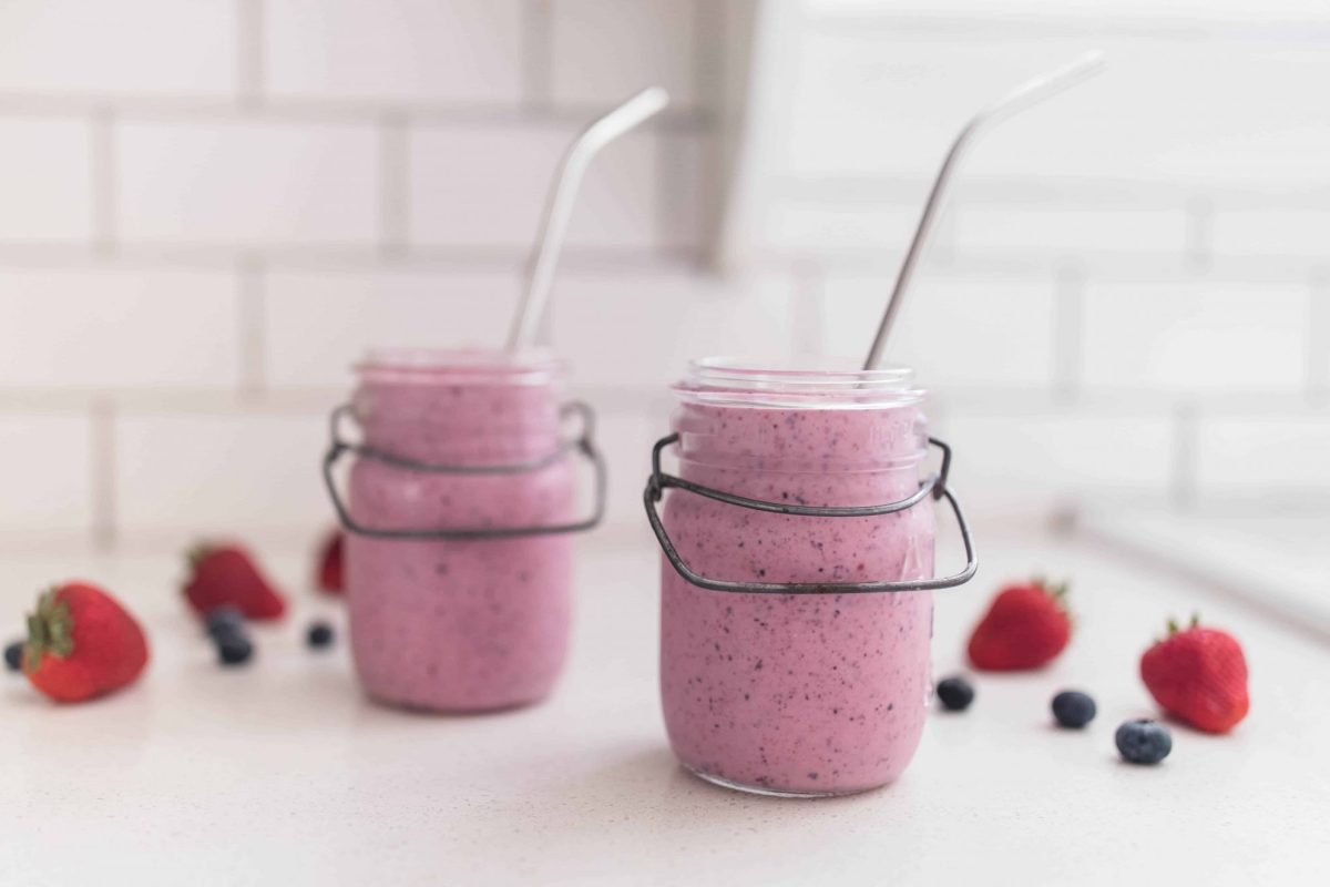 two jars of berry kefir smoothie on a counter with berries around 