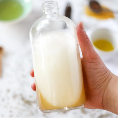 hand holding a bottle of natural homemade bubble bath with ingredients in the background