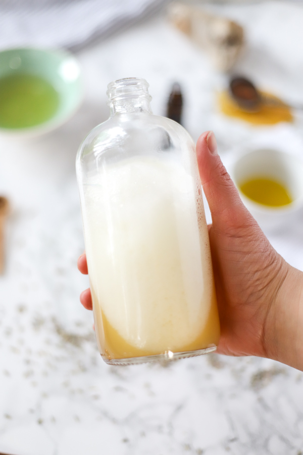 hand holding a bottle of natural homemade bubble bath with ingredients in the background