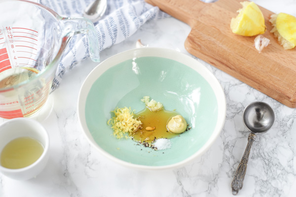 bowl of lemon vinaigrette dressing ingredients including lemon zest, honey, dijon mustard, and garlic