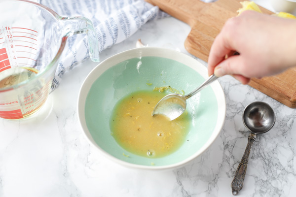 mixing lemon vinaigrette dressing together in a teal bowl on a marble countertop