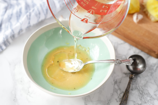 adding olive oil to a bowl of other ingredients to make homemade lemon vinaigrette dressing