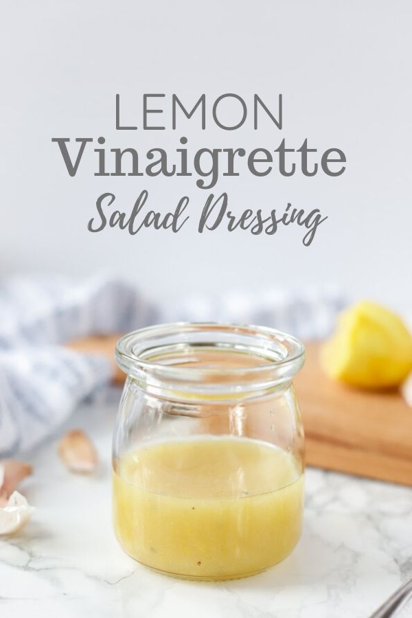lemon vinaigrette salad dressing in a glass jar with a cutting board with sliced lemons. Garlic cloves and a towel are in the background
