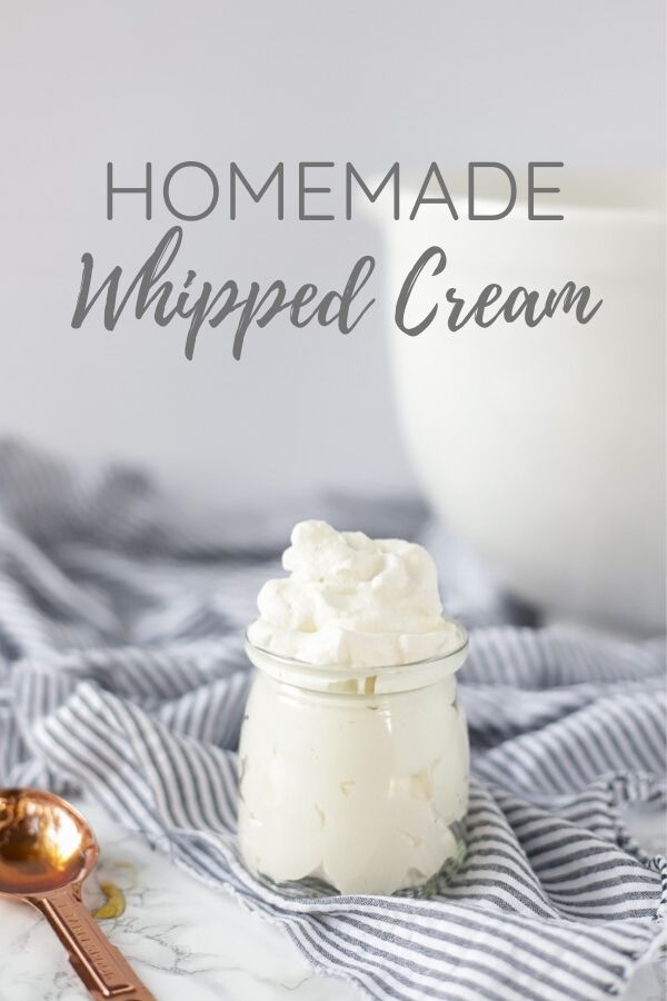 homemade whipped cream in a glass jar on a stripped towel with a copped spoon to the right and large white bowl in the background