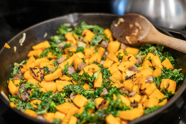 sweet potatoes, sausage, and kale cooking in a cast iron skillet