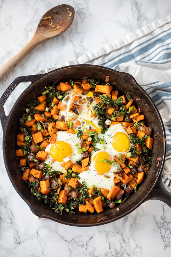 overhead shot of sweet potato hash with sausage and kale and topped with eggs in a cast iron skillet