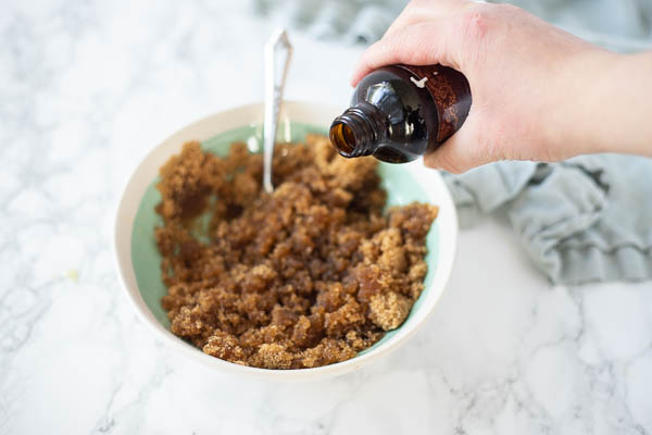 pouring vanilla extract into brown sugar and oil in a bowl on a white countertop