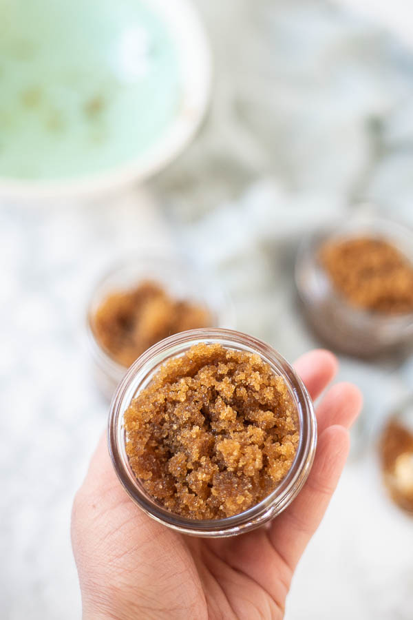 hand holding a jar of brown sugar scrub with more scrub in the background