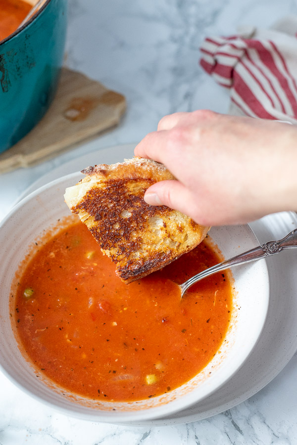 sourdough grilled cheese being dunked into homemade tomato soup